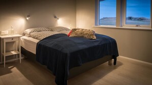 A bedroom with a bed, bedside table, and a window with a view of the outdoors. - Bryggjur (Rangárþing eystra)
