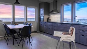 A modern kitchen with a dining area, large windows with a view, and a high ceiling. - Bryggjur (Rangárþing eystra)