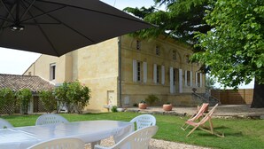 A patio with a table and chairs, a hammock, and a building with a tiled roof in the background.