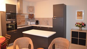A modern kitchen with dark cabinetry, a central island, a microwave, oven, and a coffee maker. There is a clock on the wall and a vase with flowers on the counter.