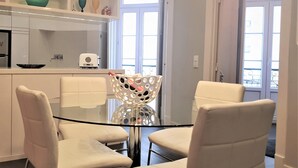 Una cocina moderna con armarios blancos, una mesa de comedor de superficie de vidrio y sillas blancas.