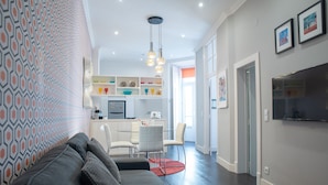 Una sala de estar moderna con un sofá gris, un tapete rojo y una cocina al fondo.