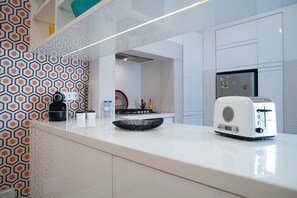 A modern kitchen with a white countertop, a toaster, a kettle, and a coffee maker.