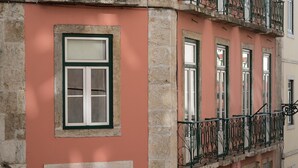 Un edificio con fachada rosa, base de piedra y un balcón con barandilla de hierro forjado.