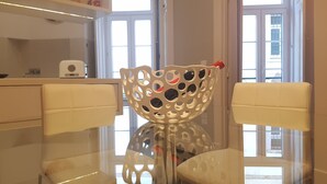 Un comedor con una mesa de vidrio, dos sillas blancas acolchadas y un cuenco decorativo blanco como centro de mesa.