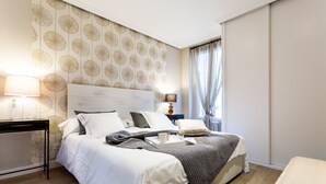 A neatly arranged bedroom with a large bed, bedside tables, and a window with curtains.