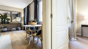 A modern living room with a dining area, wooden flooring, a large mirror, and a view through a doorway.