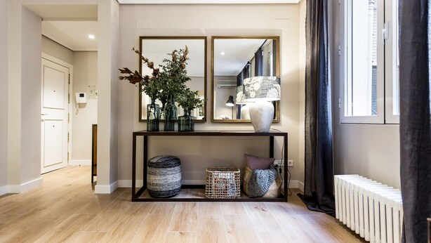 A modern hallway with a wooden floor, a console table with decorative items, a mirror, and a radiator.