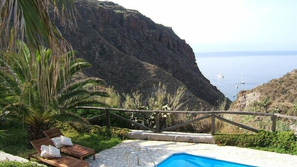 A pool with a stone deck, wooden lounge chairs, and a view of the sea and cliffs. - Aeolian Island Villa-Detached villa LIPARI, private pool with stunning sea view (Lipari)