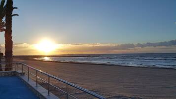 Une plage avec un coucher de soleil, des palmiers et une rambarde.