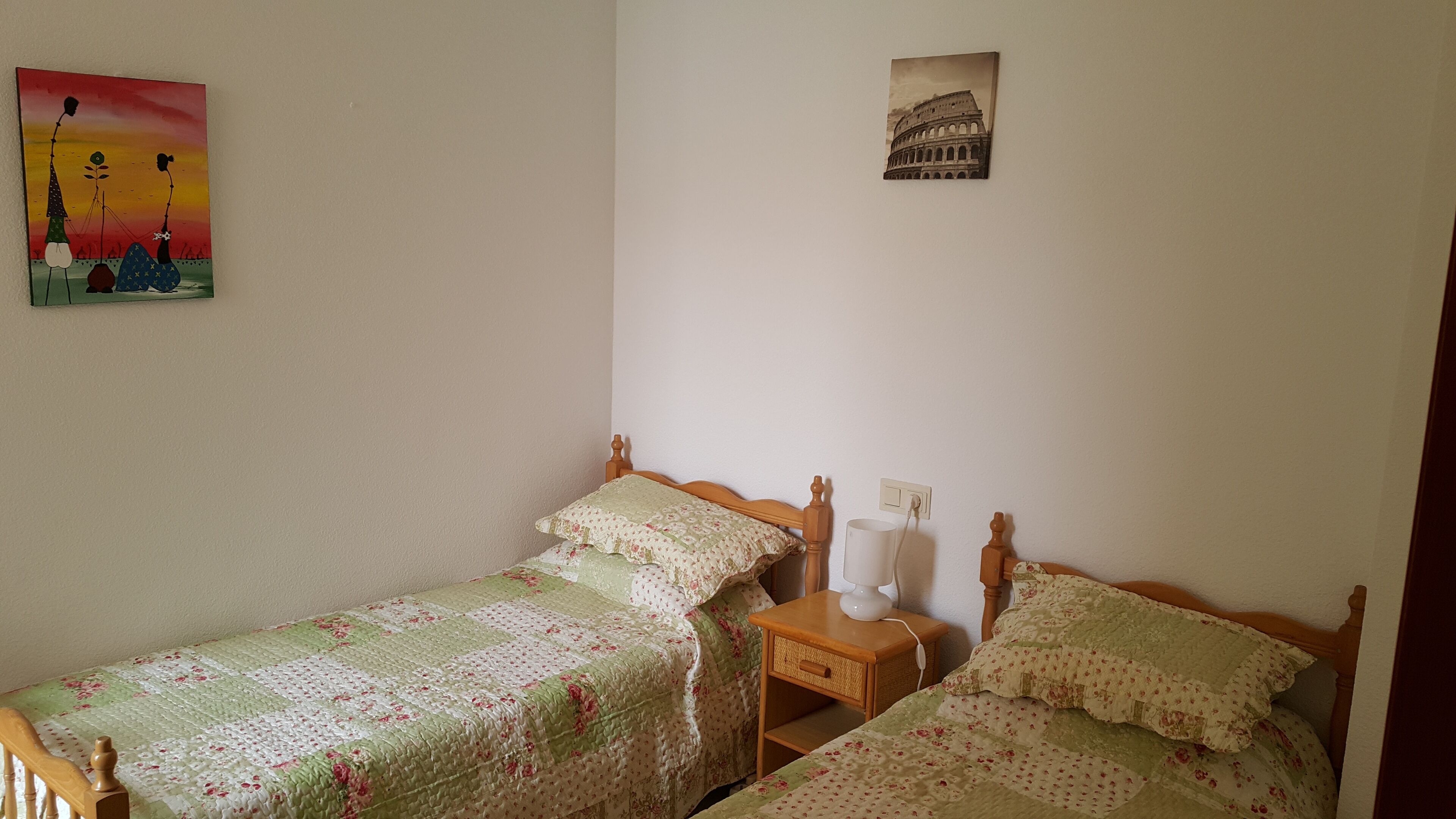 Une chambre avec deux lits simples, une table de chevet avec une lampe et un tableau représentant le Colisée, accroché au mur.