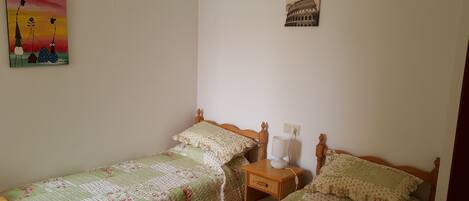 Une chambre avec deux lits simples, une table de chevet avec une lampe et un tableau représentant le Colisée, accroché au mur.