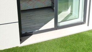 Een moderne kamer met een bed, een stoel en een klein tafeltje. Er is een schuifdeur van glas die leidt naar een buitenruimte.