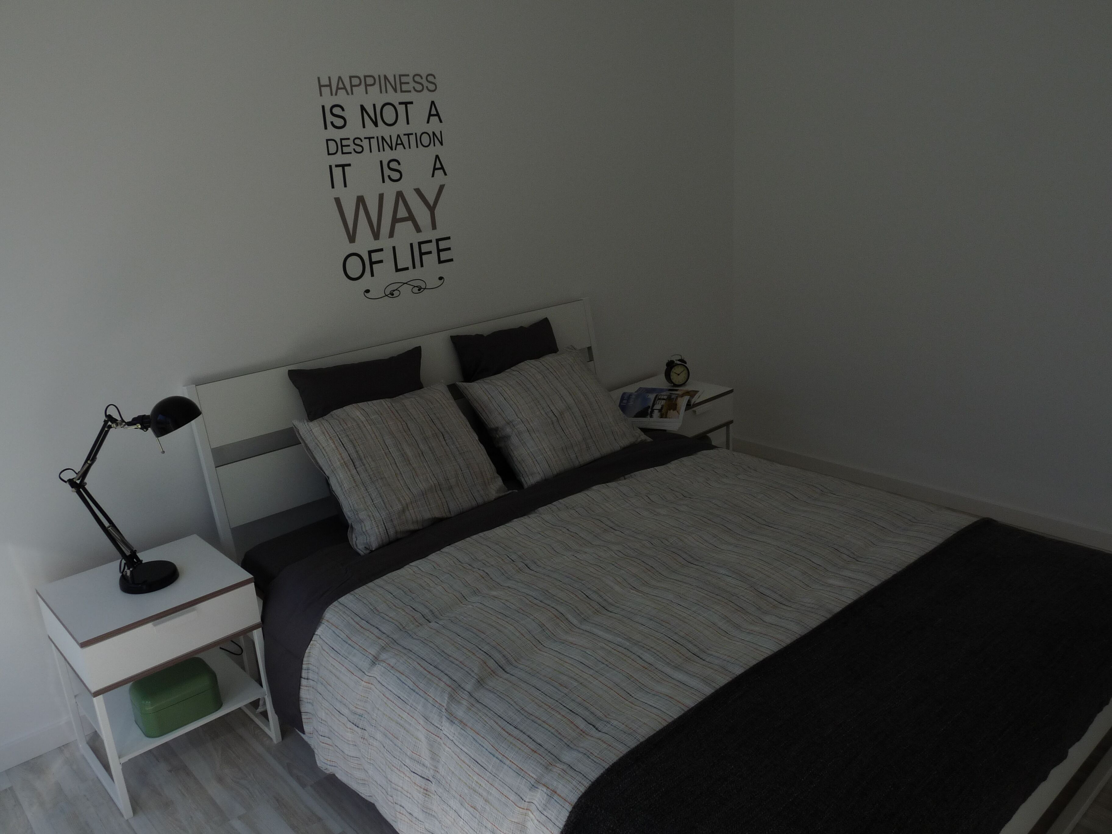 A bedroom with a bed, a nightstand, a lamp, and a wall with a motivational quote.