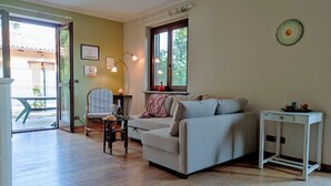 Una sala de estar con sofá, sillón, mesa y lámpara. Se ve una ventana con vistas a árboles.