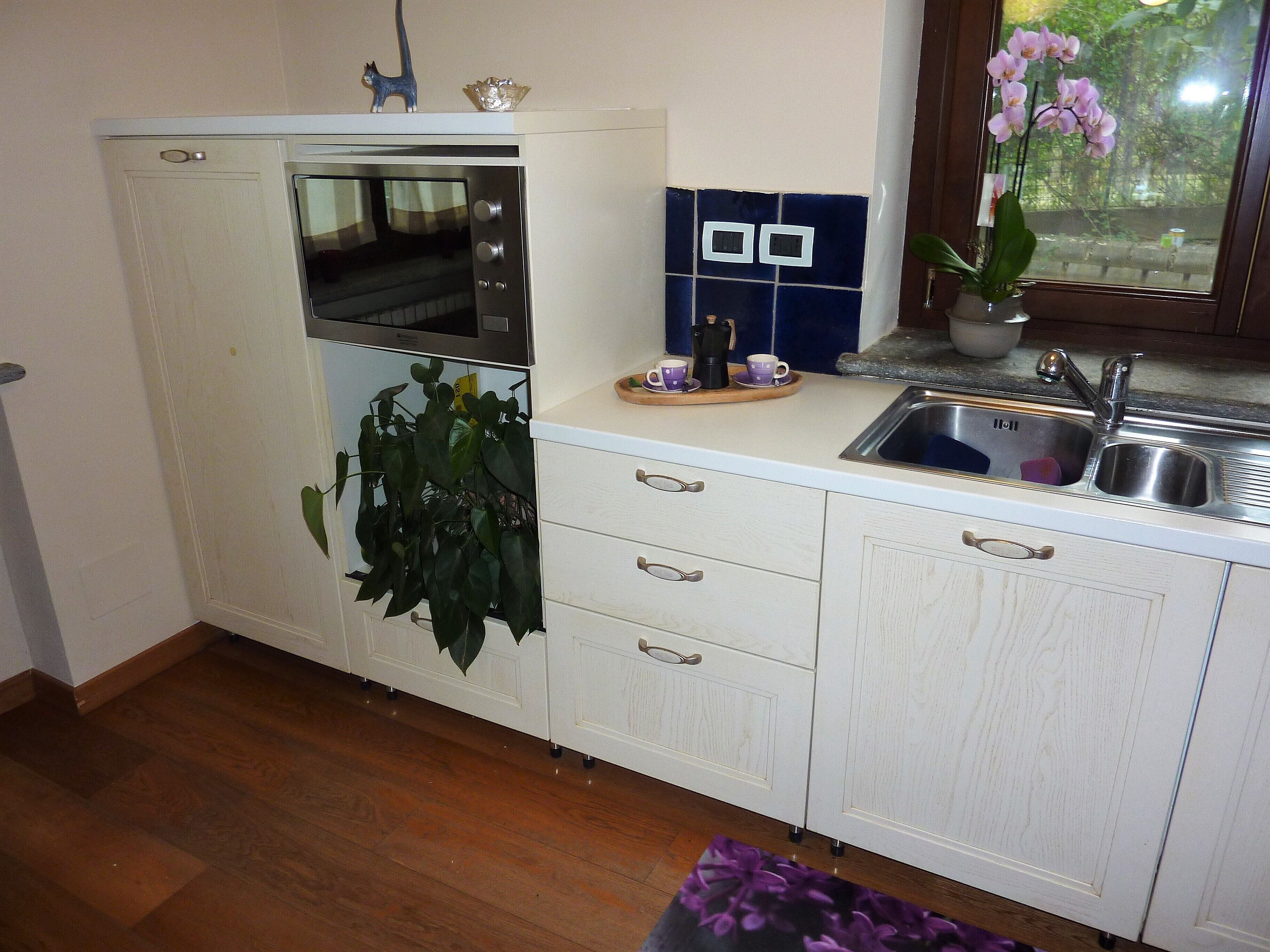A kitchen with white cabinets, a built-in oven, a sink, and a window with a view of greenery outside.