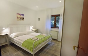 A bedroom with a bed, bedside table, window, and a painting on the wall.