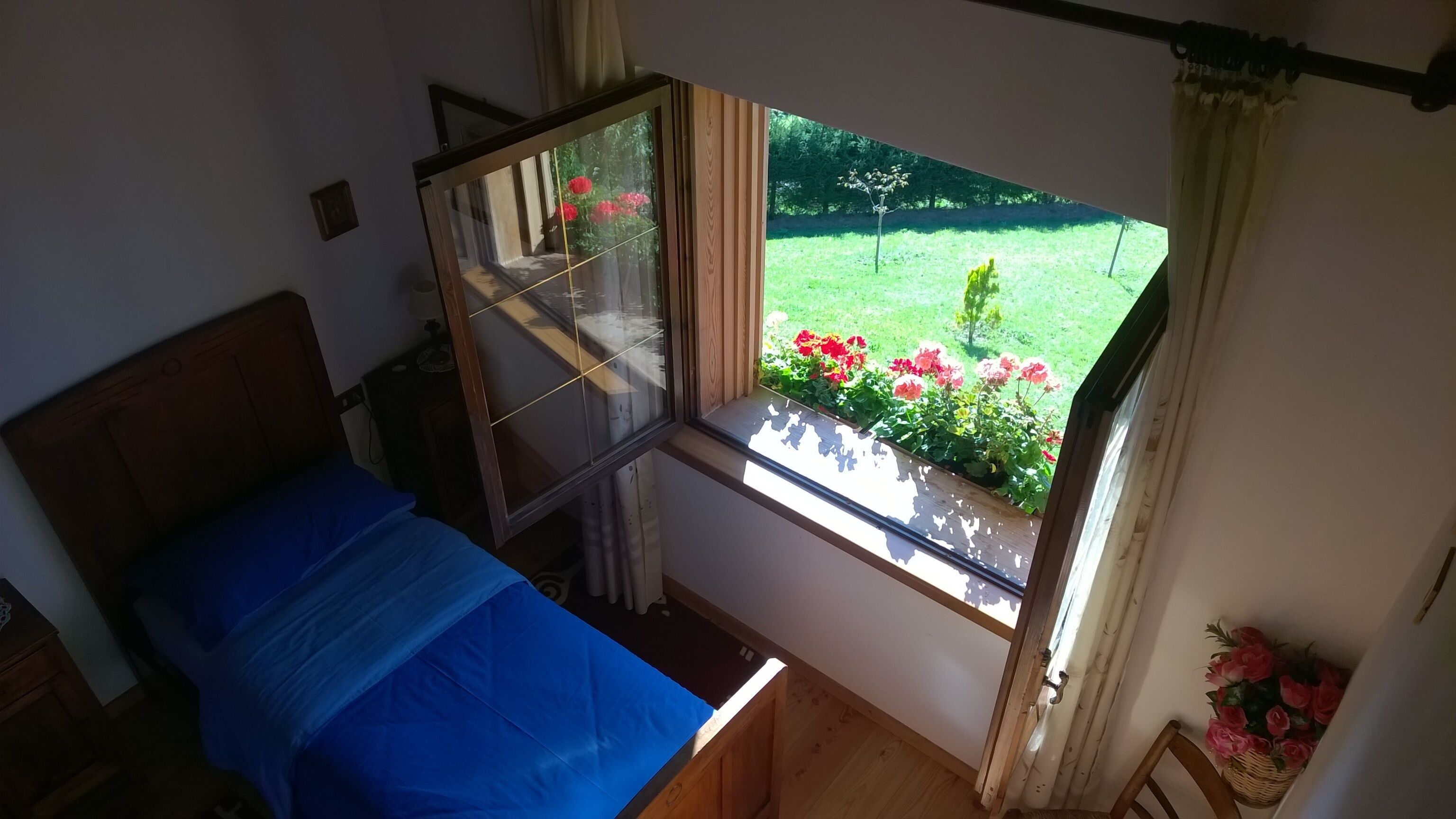Une chambre à coucher avec un lit, une fenêtre donnant sur un jardin et une tête de lit en bois.