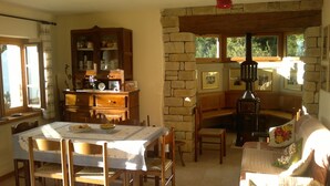 A cozy dining area with a table set for two, wooden chairs, a cabinet with dishes, and a stone fireplace.