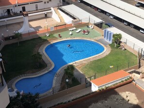 A swimming pool with a curved design, surrounded by a fenced area with lounge chairs and a small grassy section.