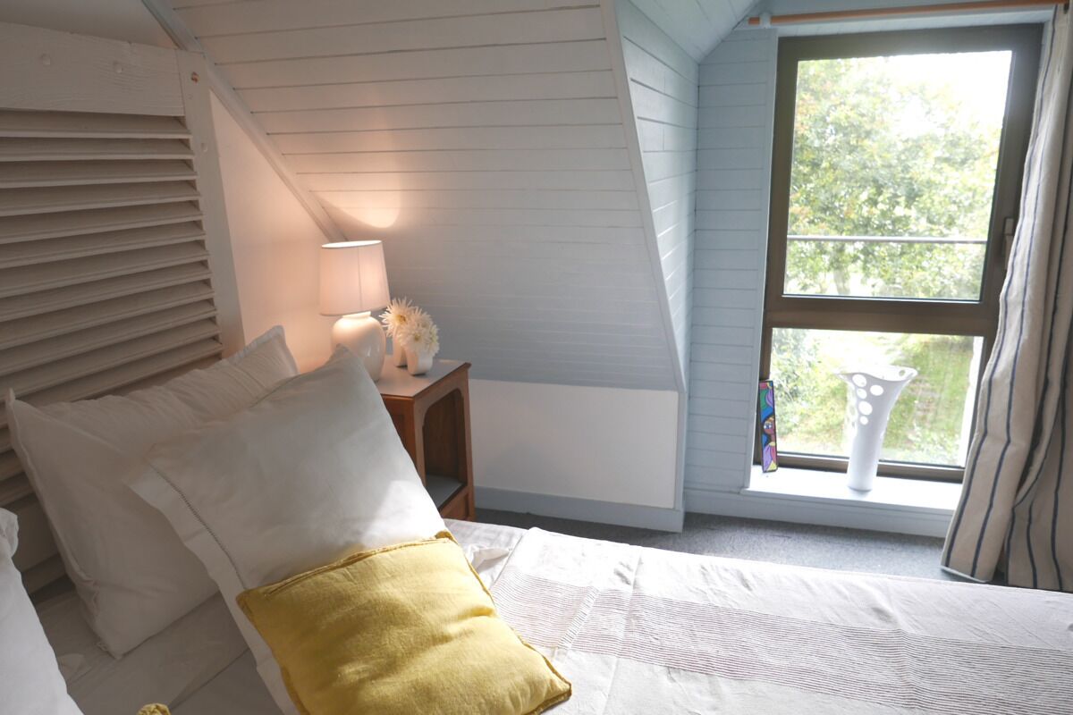 A bedroom with a bed, a nightstand, a lamp, and a window with a view of greenery.