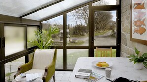 A conservatory with a table, chairs, a plant, and a view of the outside.