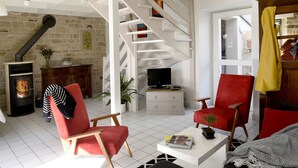 A cozy living room with a fireplace, a red chair, a television, and a staircase leading to another level.