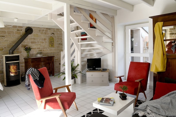 A cozy living room with a fireplace, a red chair, a television, and a staircase leading to another level.
