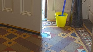 Una habitación con una puerta, un recogedor azul, un cubo amarillo y un cubo de metal sobre el suelo.