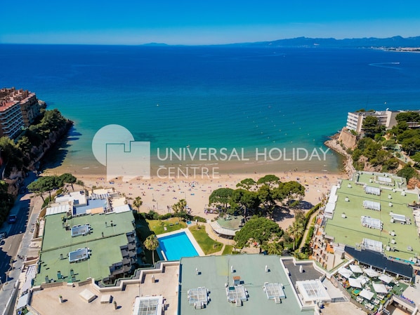 An aerial view of a beach resort with a swimming pool, beach, and ocean.