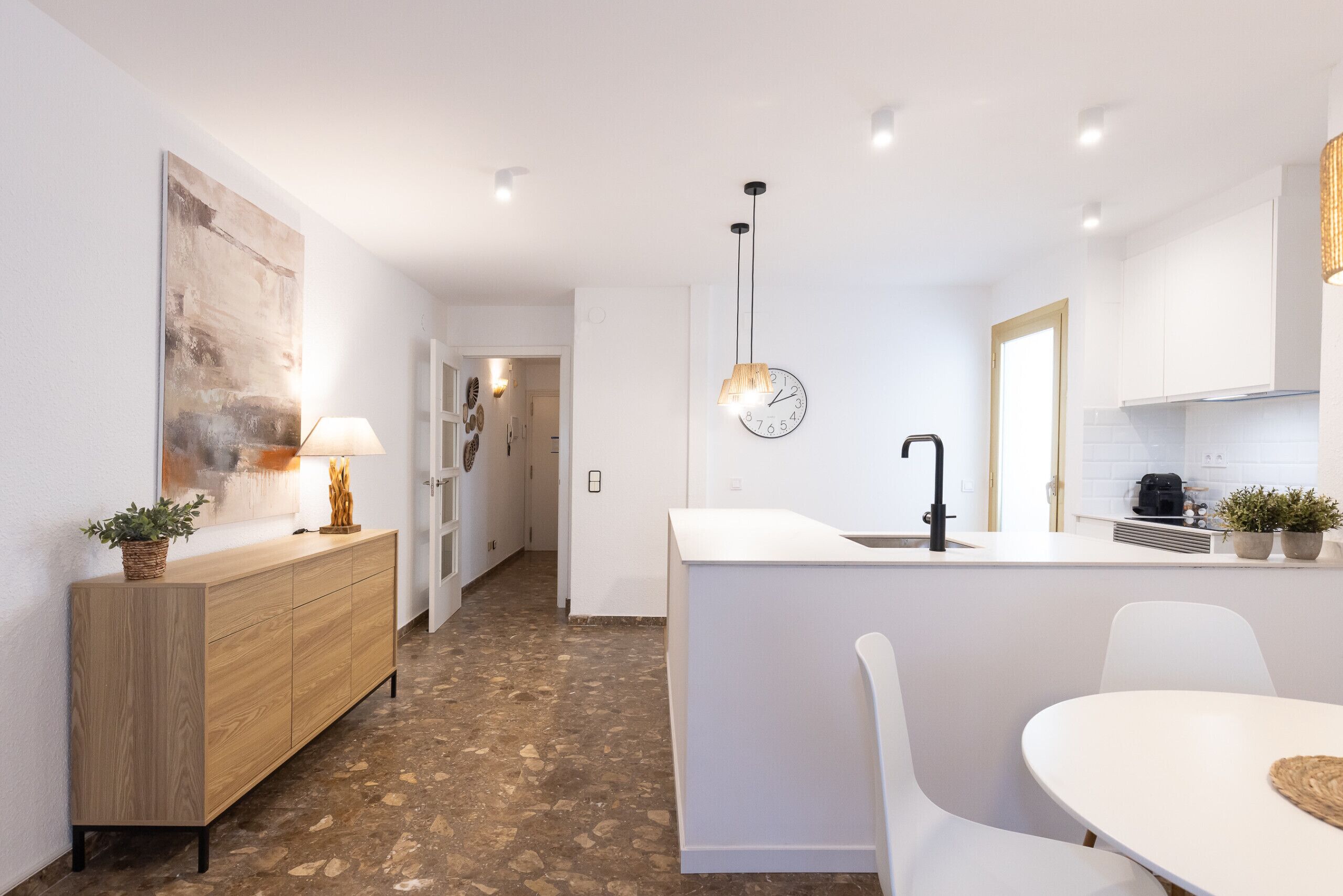 A modern kitchen with a white countertop, a clock, and a pendant light.