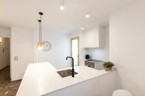 Eine moderne Küche mit weißer Arbeitsplatte, einem schwarzen Wasserhahn, einer Pendelleuchte und einer Uhr an der Wand.