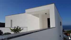 Un bâtiment moderne, de couleur blanche, doté d’un toit plat, d’un petit balcon et offrant une vue sur la mer.