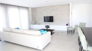 Un salon moderne comprenant un canapé, une table basse, un téléviseur fixé au mur et un coin repas avec des chaises et une table.