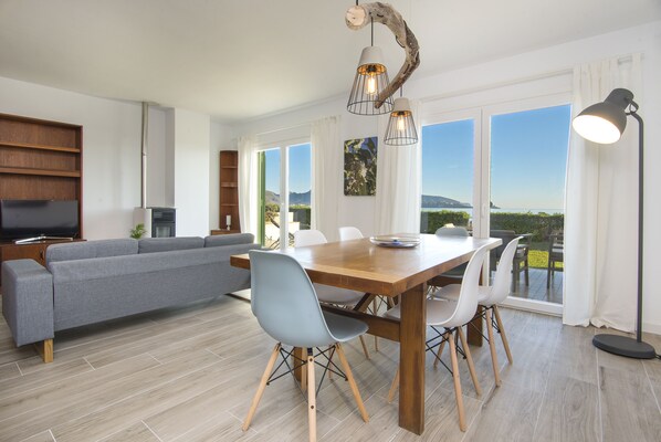 A modern living room with a grey sofa, wooden dining table, and chairs. There is a TV, a plant, and artwork on the walls. - Ground Floor in the middle of Pollensa Bay (Puerto Pollensa)
