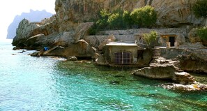 Un bâtiment situé sur la côte, doté d’une petite entrée et d’un escalier menant à sa porte, et se trouvant à proximité d’une eau turquoise et cristalline.
