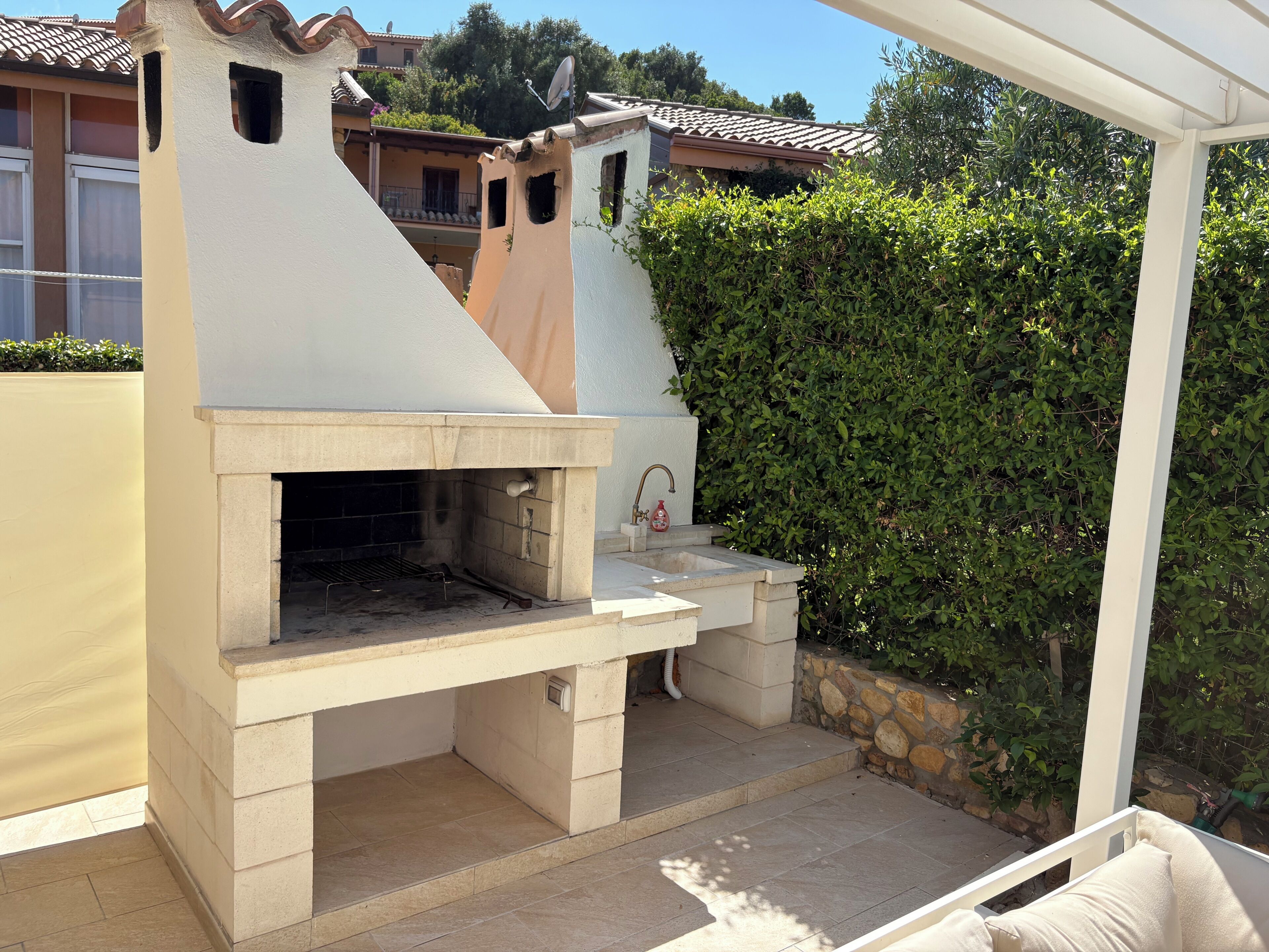 Una cocina exterior con una parrilla, un lavamanos y una pared de piedra.