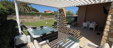 An outdoor patio with a hot tub, seating, and a stone wall.