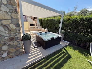A stone wall, a hot tub, a covered seating area, and a well-maintained lawn.