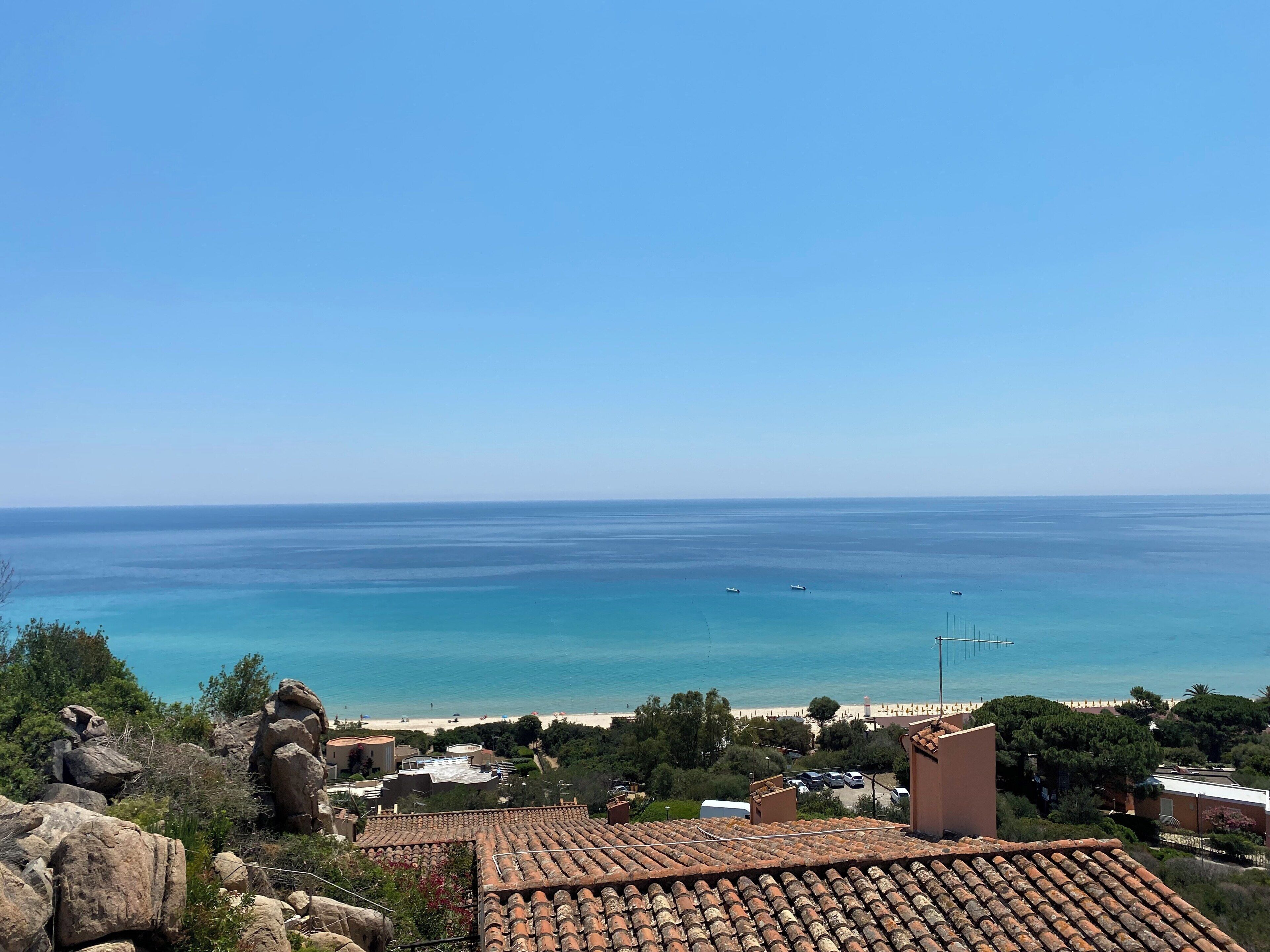 Un paese costiero con tetti in terracotta, una spiaggia e un cielo azzurro limpido.