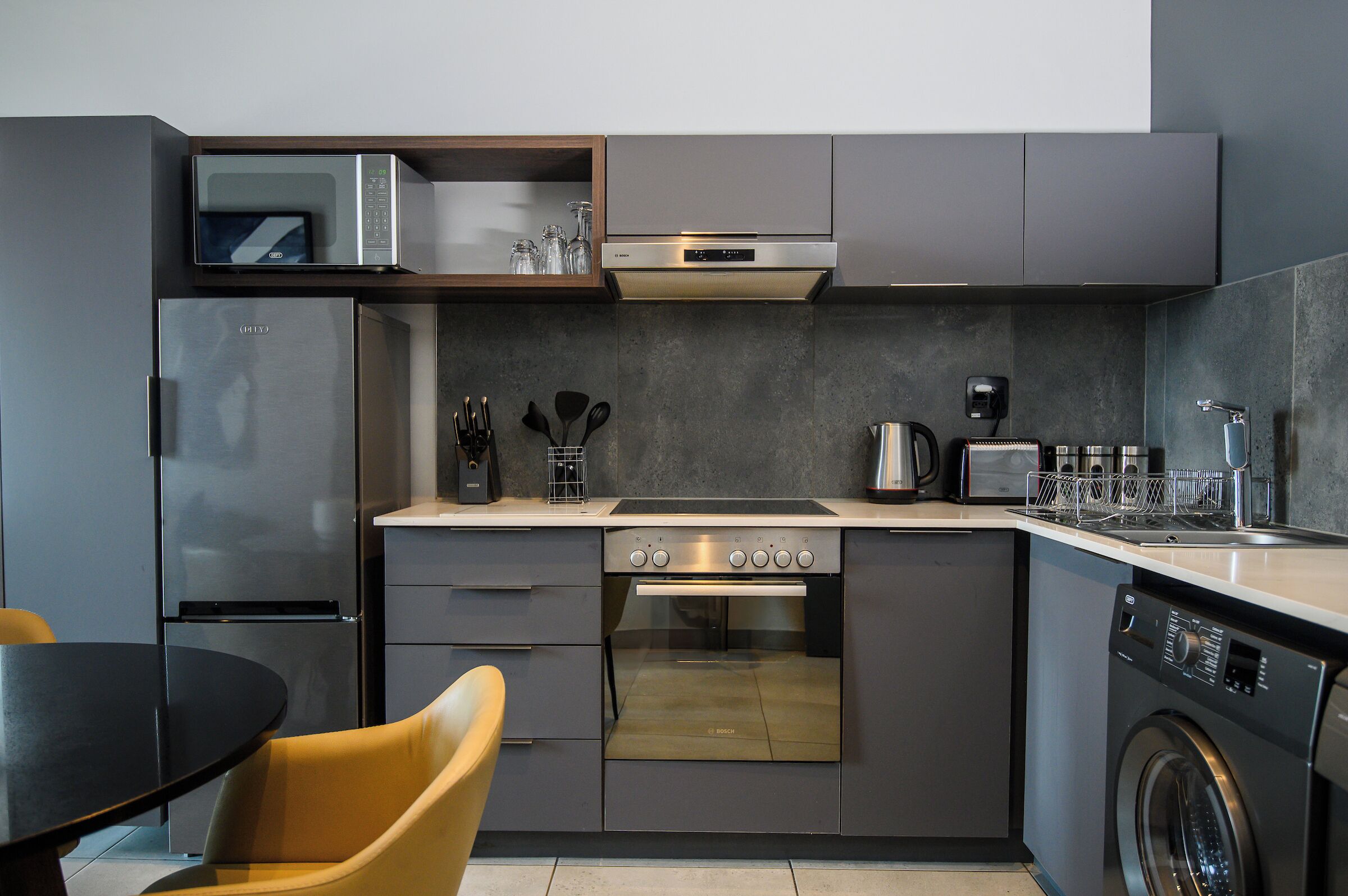 A compact kitchen with a built-in oven, microwave, and dishwasher, featuring modern appliances and a minimalist design.