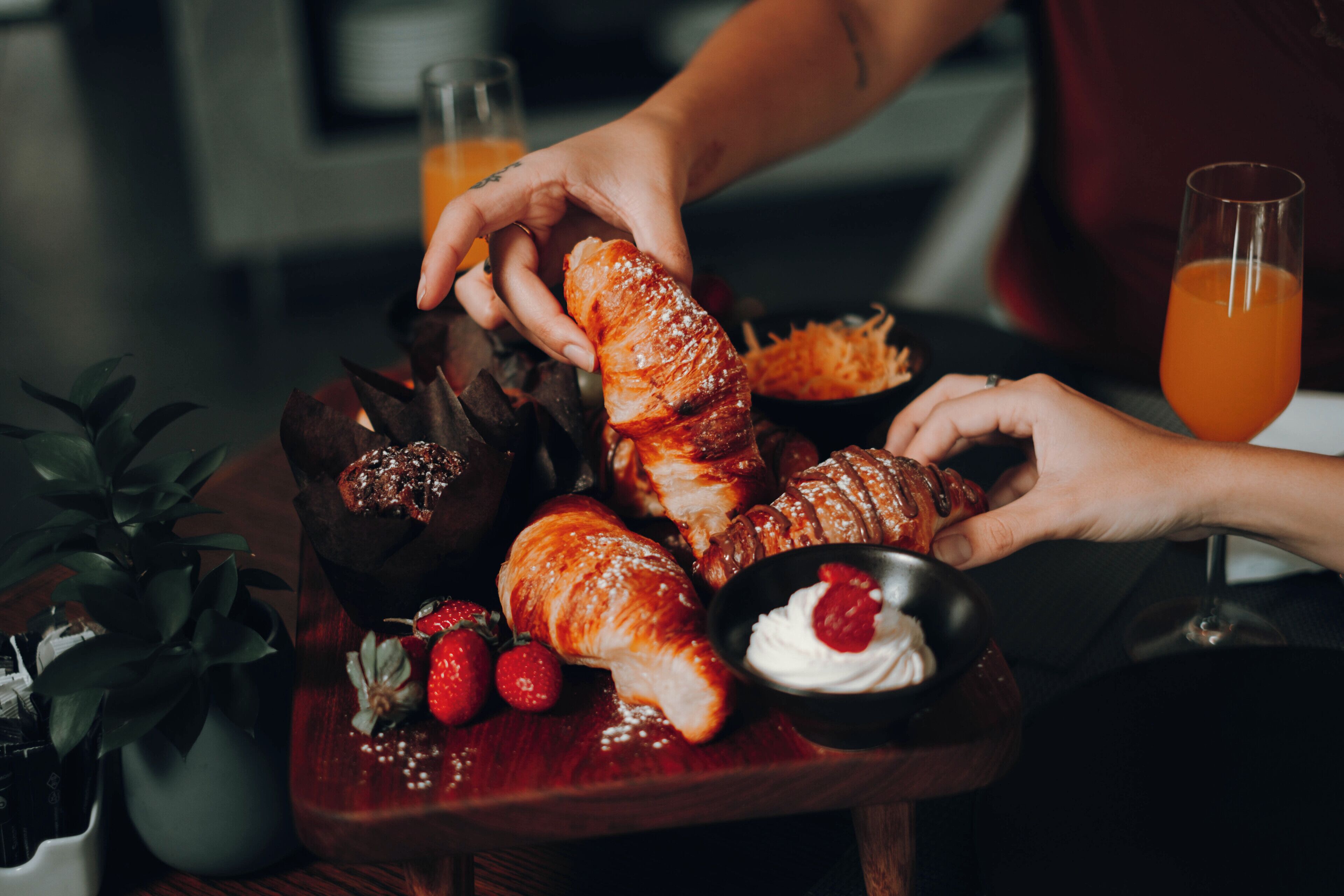 A wooden board with pastries, strawberries, and a bowl of whipped cream.