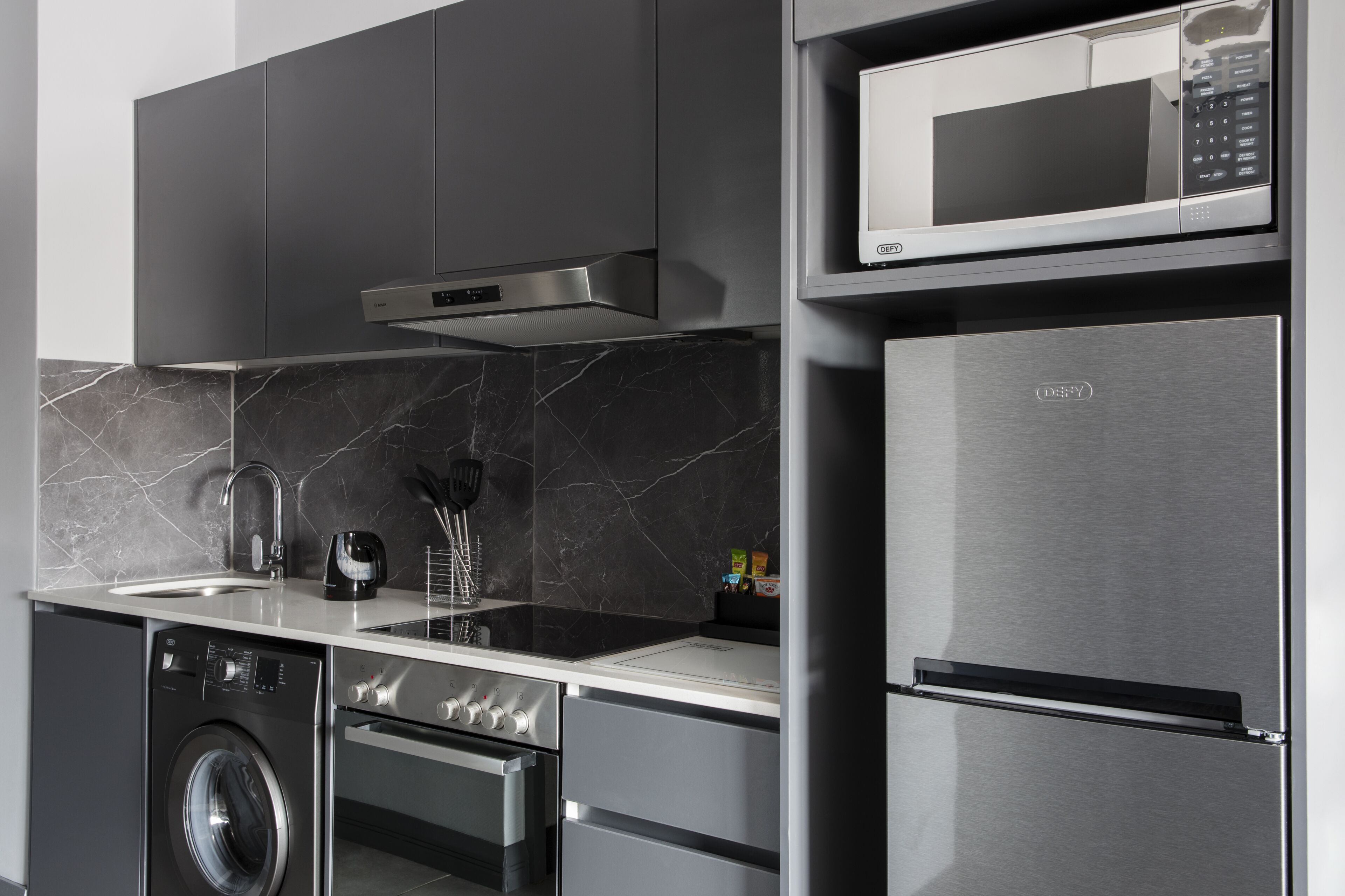 Una cocina moderna con electrodomésticos de acero inoxidable, lavadora integrada y microondas.