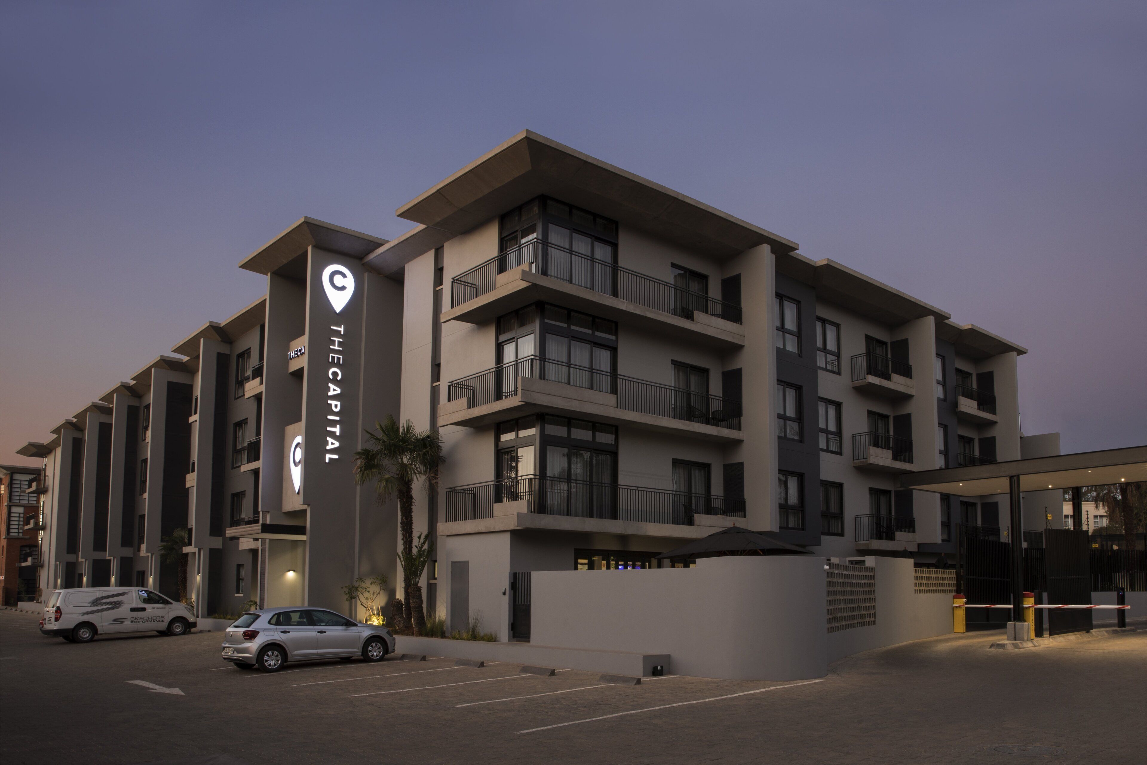 A multi-story hotel with a prominent 'The Capital' sign, a parking lot, and a gated entrance.