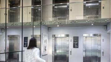 Un vestíbulo moderno con paredes de vidrio, varios ascensores y una zona con bancos verdes.