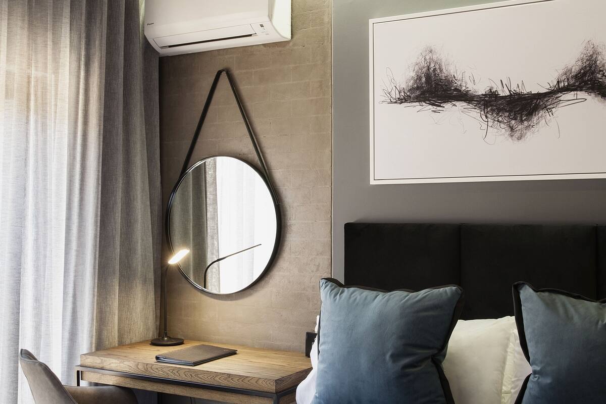 Een moderne hotelkamer met een bed, een bureau met stoel, een ronde spiegel en een groot abstract schilderij aan de muur.