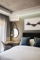 Una habitación de hotel moderna con una cama, un escritorio con una silla, un espejo redondo y un cuadro abstracto grande en la pared.