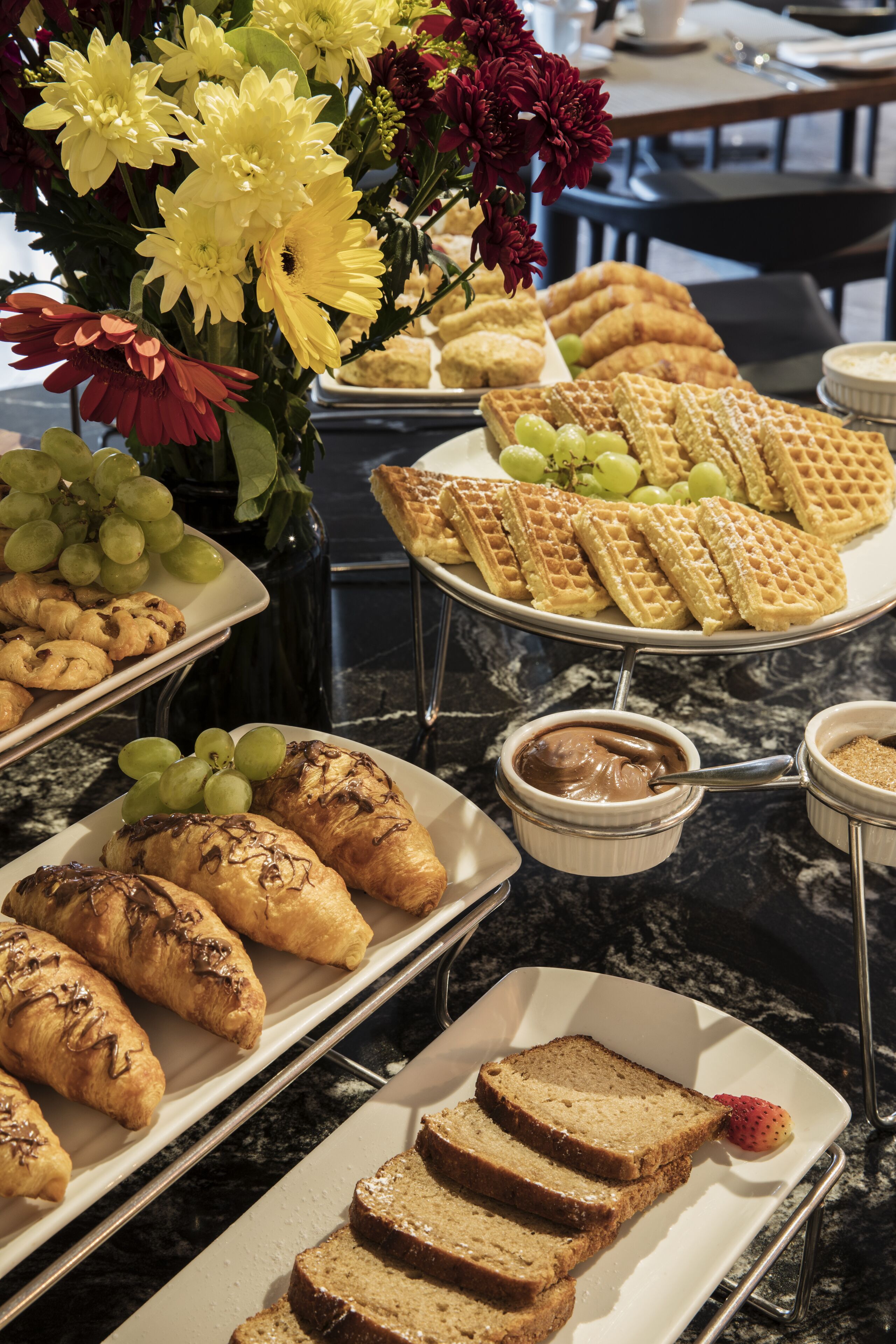 Buffet com diversos itens de comida, incluindo waffles, pastelaria e uma seleção de frutas.
