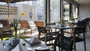 Een restaurant met terras, tafels gedekt met witte servetten en gele bloemen in vazen.