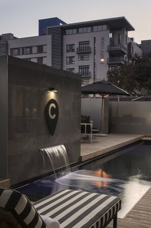Un hôtel moderne doté d’une piscine, de chaises longues et d’un élément décoratif aquatique.